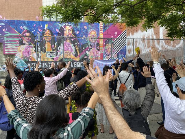 People holding their hands up in front of a painted memorial